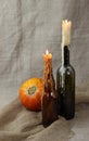 Halloween autumn still life. Pumpkin, candles in bottles, herbs. Light canvas background.
