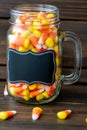 Halloween background frame consisting of a jar full of candy corn on a dark wooden table with a black table that you can personali Royalty Free Stock Photo