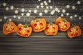 Halloween background with pumpkins with creepy cut out faces and hanging garland bulb lights over wooden board.