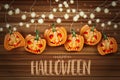 Halloween background with pumpkins with creepy cut out faces and hanging garland bulb lights over wooden board.