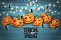 Halloween background with pumpkins with creepy cut out faces and hanging garland bulb lights and spiders over blue wooden board ba