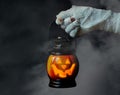 Halloween background. Zombie hand holding a lantern in the form of a pumpkin on a smoky dark background. Halloween design Royalty Free Stock Photo