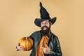 Halloween beaded man hold pumpkin - portrait. Scary hipster man with beard in Halloween hat. Handsome man in Halloween