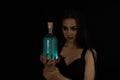 For Halloween, a beautiful witch brewed a potion. On a black background, a woman witch holds a bottle of poison in her Royalty Free Stock Photo