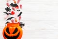 Halloween candy with skulls, black bats, ghost, spider decorations spilled from jack o lantern bucket on white wooden background, Royalty Free Stock Photo