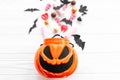 Halloween candy with skulls, black bats, ghost, spider decorations spilled from jack o lantern bucket on white wooden background, Royalty Free Stock Photo