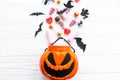 Halloween candy spilled from jack o lantern bucket with skulls, black bats, ghost, spider decorations on white wooden background, Royalty Free Stock Photo