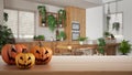 Halloween carved pumpkins on wooden table. Autumn decoration over interior design scene. Wooden modern kitchen with houseplants, Royalty Free Stock Photo