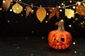 Halloween ceramic jack lantern, leaves garland and bokeh lights on black background. Greeting card Royalty Free Stock Photo