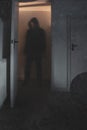 A Halloween cocept of a blurred scary, hooded figure, standing in a doorway. with a knife. With a vintage, abstract edit