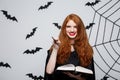 Halloween Concept - Beautiful Witch playing with magic stick and magic book on grey background. Royalty Free Stock Photo