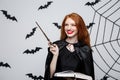 Halloween Concept - Beautiful Witch playing with magic stick and magic book on grey background. Royalty Free Stock Photo