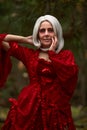 Halloween concept, glamorous costume detail. Young beautiful and mysterious woman in woods, in white Dress and Red Cloak Royalty Free Stock Photo