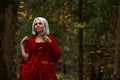 Halloween concept, glamorous costume detail. Young beautiful and mysterious woman in woods, in white Dress and Red Cloak Royalty Free Stock Photo