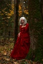 Halloween concept, glamorous costume detail. Young beautiful and mysterious woman in woods, in white Dress and Red Cloak Royalty Free Stock Photo