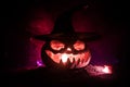 Halloween concept. Jack-o-lantern smile and scary eyes for party night. Close up view of scary pumpkin with witch hat on at dark f Royalty Free Stock Photo