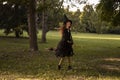 Little girl in witch costume and black long hat holding wooden broom, standing outdoor against autumn forest background. Royalty Free Stock Photo