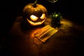 Halloween during Corona virus global pandemic concept. Glowing pumpkins and Covid novel on dark with thematic spooky decorations.