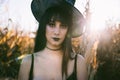 Halloween costume witch girl portrait in a cornfield at sunset. Beautiful serious young woman in witches hat with long black hair Royalty Free Stock Photo