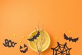 Halloween creative greeting card. Paper decorations, plate, tree branch and pumpkin on orange background. Top view, flat lay