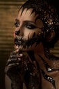 Halloween and creative make-up theme: beautiful girl model with black body with gold mask skull paint on dark background in studio Royalty Free Stock Photo