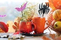 Halloween decor, a couple of cups with a drink, spiders, pumpkins, fruits, leaves on the windowsill, autumn seasonal holidays