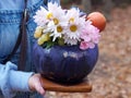 Halloween decoration, flower and fruit bouquet in a vase of painted pumpkin in female hands