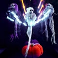 Halloween decoration three skeletons in a multicolored cape decorated with a garland of glowing pumpkins and spiders. The light of