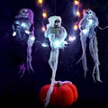 Halloween decoration three skeletons in a multicolored cape decorated with a garland of glowing pumpkins and spiders. There is a