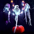 Halloween decoration three skeletons in a multicolored cape decorated with a garland of glowing pumpkins and spiders. There is a