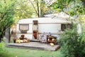 Interior cozy yard campsite with flowers potted and pumpkins. Wooden RV house porch with garden furniture.