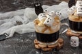 Halloween drink. Two cups coffee with marshmallow spooky faces, monster, bats on dark background