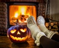 Halloween eve. Female feet in soft wool socks and burning fire in fireplace at the background