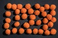 Halloween festive background. Randomly scattered orange fluffy pom-poms on a black background. Top view. Copy space