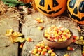 Halloween festive composition with sweet corn in bowl and smiling pumpkins guards, lantern, straw and fallen leaves on dark Royalty Free Stock Photo