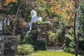 Halloween ghost decoration hanging from tree by garden gate with sun speckled and hokeh fall foliage around it