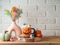 Halloween holiday celebration with jack o lantern coffee cup, modern vase and decoration on wooden table over brick wall