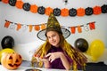 Halloween holiday concept. Cute little girl in witch costume sitting behind a table in Halloween theme decorated room Royalty Free Stock Photo