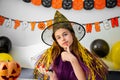 Halloween holiday concept. Cute little girl in witch costume sitting behind a table in Halloween theme decorated room Royalty Free Stock Photo