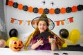 Halloween holiday concept. Cute little girl in witch costume sitting behind a table in Halloween theme decorated room Royalty Free Stock Photo