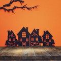 Halloween holiday concept. Empty rustic table in front of black houses village and bare tree branches background. Ready for produc