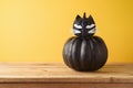 Halloween holiday creative concept with cute funny black pumpkin decor as black cat on wooden table over yellow background Royalty Free Stock Photo