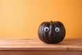 Halloween holiday creative concept with cute funny black pumpkin decor on wooden table over orange background