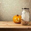 Halloween holiday decoration with ghost in jar and jack lantern pumpkin on wooden table over bokeh background Royalty Free Stock Photo