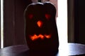 A pumpkin lantern of a fabulous monster with glowing eyes looks out of the darkness against the background of an open door