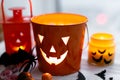 Halloween jack o lantern bucket, glowing candle, festive candy, skulls, black bats, ghost, spider decorations on white wooden
