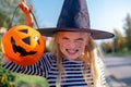 Halloween kids. Portrait Laughing girl in witch costume hat with pumpkin candy bucket on street