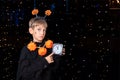 Halloween lifestyle. Boy with a spider on his cheek and a pumpkin beads holding a black alarm clock on a black