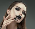 Halloween makeup. Fashion model girl with trendy gothic black make-up. Young woman smears black lipstick on her face