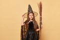 Halloween masquerade party. Childhood fascination with magic. Cute little girl with long hair wearing black witch costume and